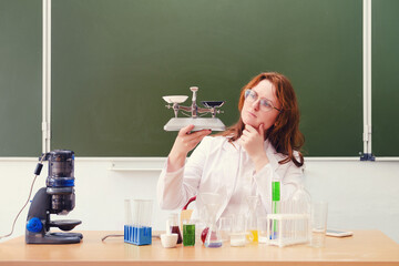 School teacher in white coat weighs on the scales while sitting at the desk. Scientific experiments...