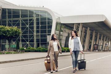 Two female co-workers returning from a joint business trip. Young women in business clothes with suitcases on the street