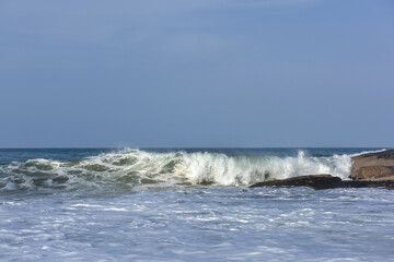 The huge waves crashing into ston island against the blue sky and horizon at summer sea shore.