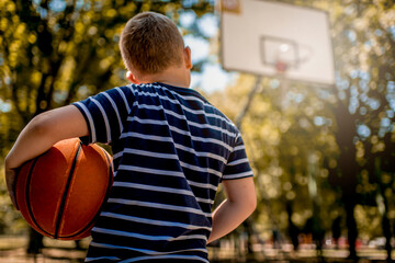 Boy holding a basketball ball at the outdoor courtyard.