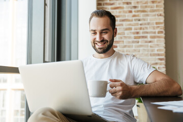 Image of man drinking coffee and using laptop while sitting at table