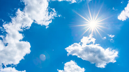 Hot summer or heat wave background, glowing sun on blue sky with clouds