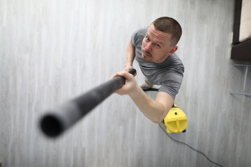 A man collects dust from the ceiling with a vacuum cleaner. The tool sucks in dust and debris on...