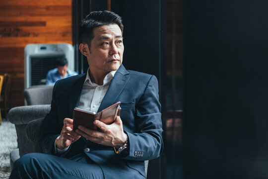 Focused businessman in a stylish suit and white shirt sits in a cafe with a phone in his hand and look aside stock photo