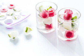 Cocktail glasses with berries in ice cubes on white table