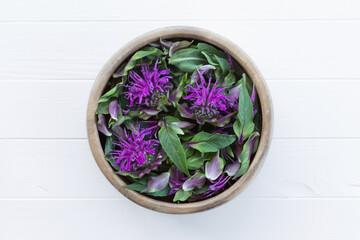 Monarda in a wooden bowl. Flowers and leaves of bergamot on a white wooden table. Oswego tea. Concept of edible flowers.