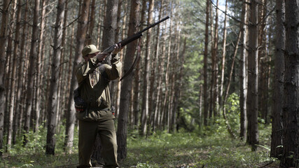 Man takes aim while standing from hunting rifle. Man in comfortable camouflage clothes hunter...