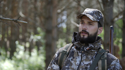Portrait of handsome young man hunter or tourist. Man in camouflage clothes hunts outdoor in forest hunting alone. Close up of man hiker standing in forest. Hunter hunts down prey.