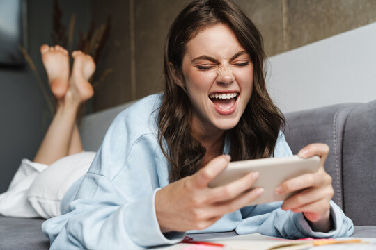 Image of woman playing online game on mobile phone while lying on sofa