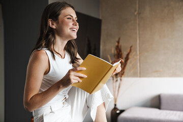 Image of joyful woman smiling and reading diary sitting in living room