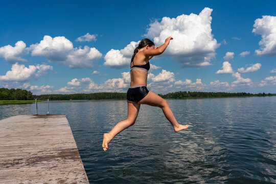 Side view of a young teenage girl jumping in to the water from a jetty with blue sky and horizon in the background.