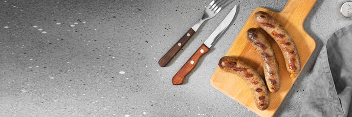 Fried sausages on a wooden serving Board on the light gray kitchen table. Fried sausages on a serving Board. Top view with space for text. Banner