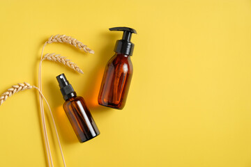 Wheat, barley and oat natural cosmetic. Flat lay amber glass shampoo bottle dispenser and spray bottle on yellow background. Top view with copy space.