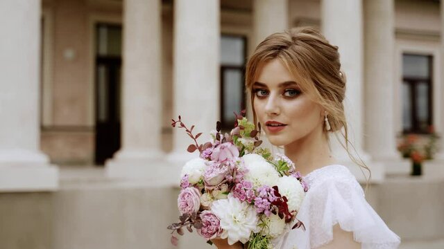 People. Beautiful bride portrait. Girl smile and looking to the camera. She has bouquet of flowers in hands. She stand near by building with stairs