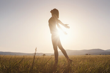 Young girl spreading hands with joy and inspiration facing the sun