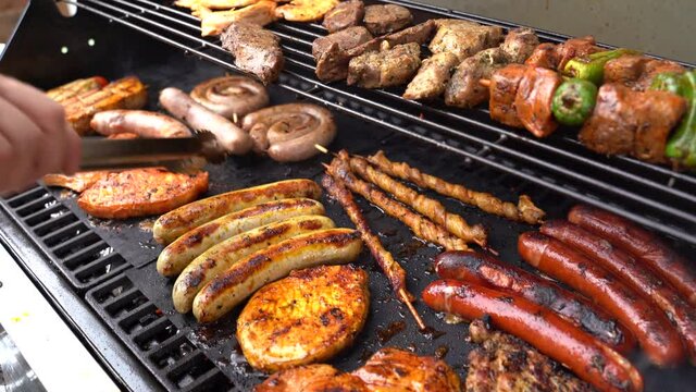 Slide right close up shot of man turing bratwurst sausages on BBQ grill in backyard during summer party