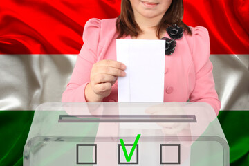 female voter lowers the ballot in a transparent ballot box against the background of the national flag of Hungary, concept of state elections, referendum