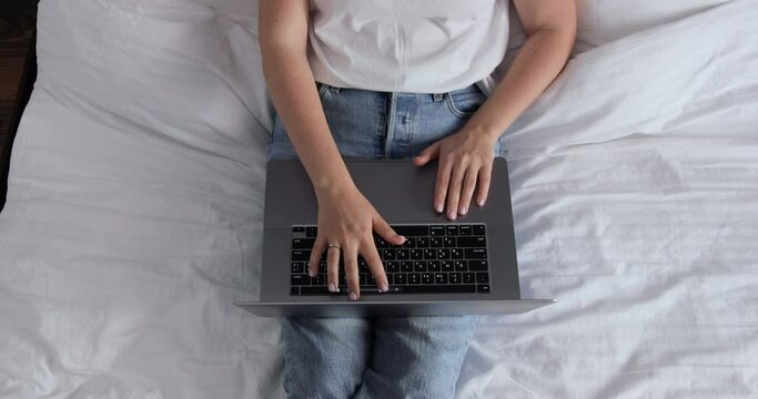 Woman in bedroom doing internet search late at night, could be student or businesswoman working from hotel room. Hands typing on MacBook Pro keyboard.