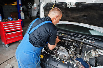 Car repair and maintenance theme. Mechanic in uniform working in auto service, checking engine.