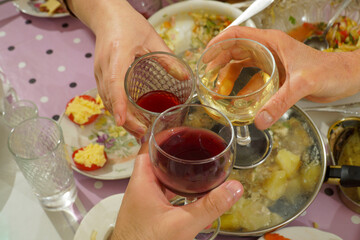 Glasses with red and white wine in three hands clink against the background of the festive table.