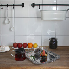 modern glass teapot with herbal tea, a glass with sliced ​​apples, berries, hawthorn flowers, fruits in the background, white kitchen, healthy eating concept, vitamin breakfast