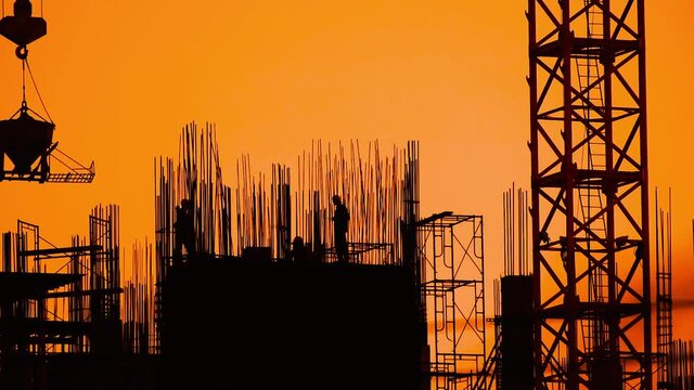 silhouette of construction workers at sunset, crane in construction site is working,binding rebar and concrete work