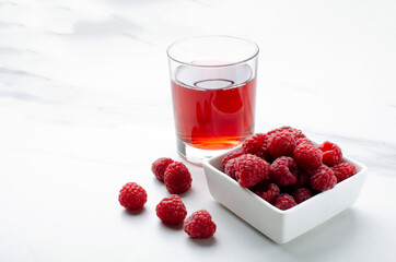 Closeup of bowl of raspberries and fresh sweet drink on the white marble surface.Empty space