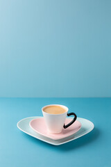 Cup of coffee on heart shaped plate on blue background. Copy space.
