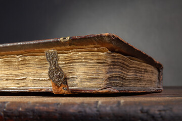 A fragment of an ancient brown book with clasps and yellow pages on an old wooden table.