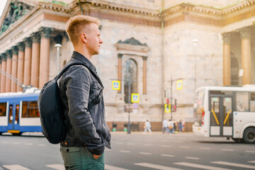 A young blond man with a backpack walks along the street next to St. Isaac's Cathedral in Saint Petersburg