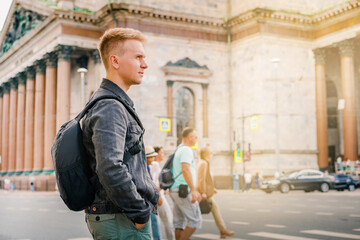 A young blond man with a backpack walks along the street next to St. Isaac's Cathedral in Saint Petersburg