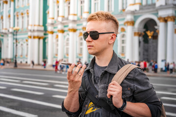 A business man in sunglasses talks on a speakerphone on a mobile phone in the center of St. Petersburg on Dvortsovaya Ploshchad