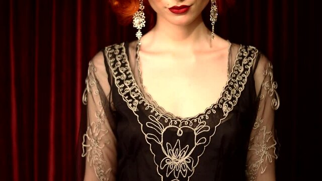 Woman smile. Lips close up. Chest and clavicle closeup. Retro woman in black vintage dress against red background in theater. Retro hairstyle. Beautiful silver earrings. 