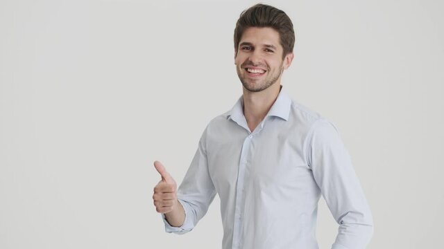 A pleased man is showing thumb-up gesture and winking isolated over white background