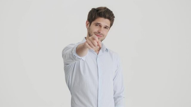A positive young man is pointing to the viewer than showing a thumb-up gesture standing isolated over white background