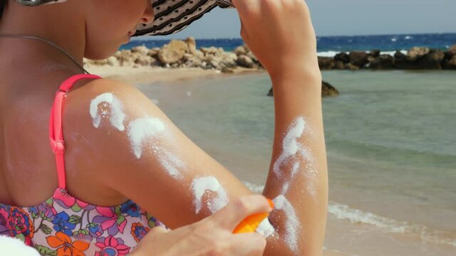 close-up, applying sunscreen or spray lotion to skin of shoulder and arm. on beach under hot sun, against backdrop of the sea. Sun and UV protection. skin protection