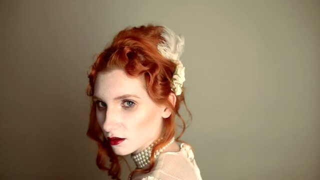 Young vampire woman portrat with blood on face turn. Scary creepy character. Pale skin demon on gray background. Redhead model with red lips. Outfit for halloween. Vampire with open mouth and fangs