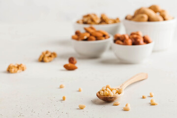 A handful of pine nuts in a wooden spoonl, assorted nuts on a light background. Healthy snacks, healthy fats. Copy space