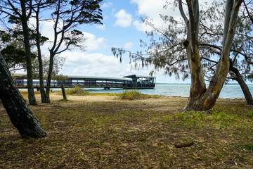 View between trees on the foreshore, to the jetty at high tide. Main Beach, Coochiemudlo Island,...