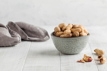 Peanuts in a shell in a gray bowl on a white wooden background. Healthy snacks, vegetable fats. Copy space.