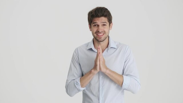 A charming man is asking for something while holding hands in a praying pose isolated over white background