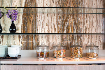 Glass jars with jelly candies, candied fruits, peanuts next to plates, on the background of brown marble wall. Snack bar