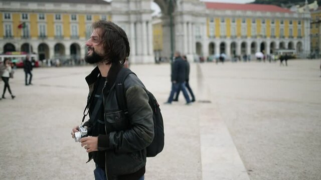 Happy male tourist standing on European square, using photo camera, taking pictures, admiring landmarks. Dolly shot. Travel concept