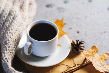 a Cup of hot coffee on the table with a knitted scarf, maple leaves and copy space