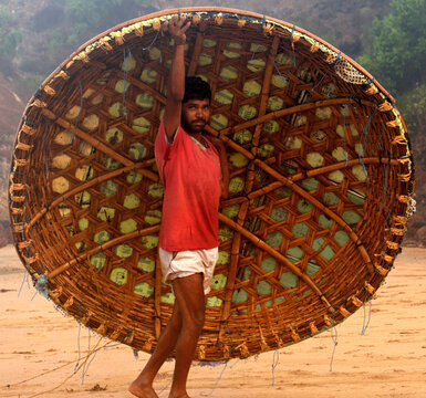 Healthy but poverty stricken, nomadic fisherman of south indian origin lifting the hand made coracle boat after his fishing shift. Satisfied with the day work and posing in a happy mood to the camera.