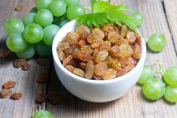 Raisins in a white dish on a wooden surface next to a bunch of white veins close up