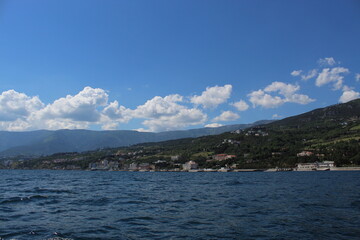 Seascape from the sea. A rocky coast that flows into the sea. Coast against the background of mountains and greenery. Clouds over the mountains