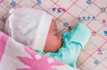 A newborn baby sleeps sweetly on its side, throwing a handle covered with a blanket. View from above