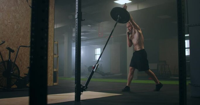 Slow motion: Man doing Single-Arm Landmine Squat-to-Press exercise. Young man lifting barbell with light weights at gym