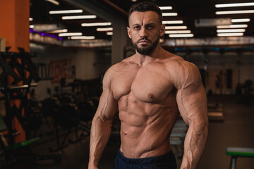 Fototapeta premium Portrait of a bodybuilder in excellent physical shape with a bare torso in the background of the gym. A man with a perfect body, a dream of any girl, a sports-obsessed man.